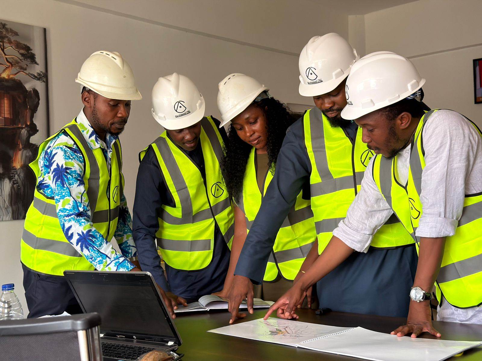 A diverse team of five engineers in safety gear examines construction plans indoors