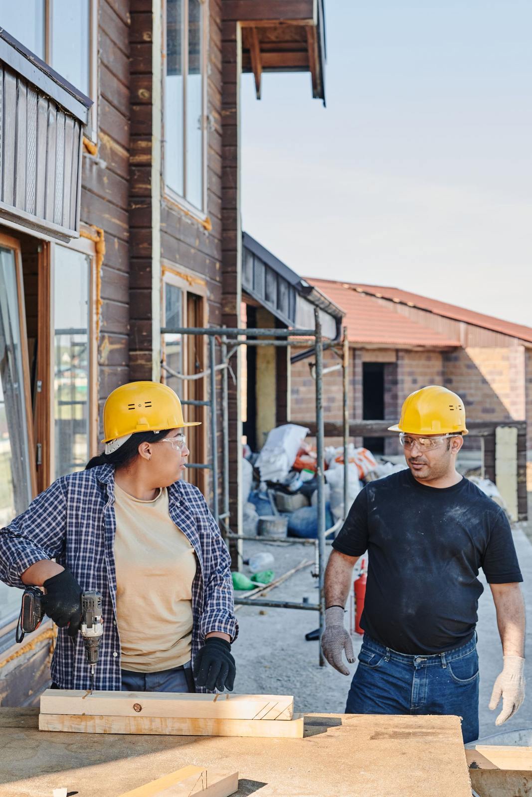 Two construction workers in safety gear discussing building plans on an outdoor construction site